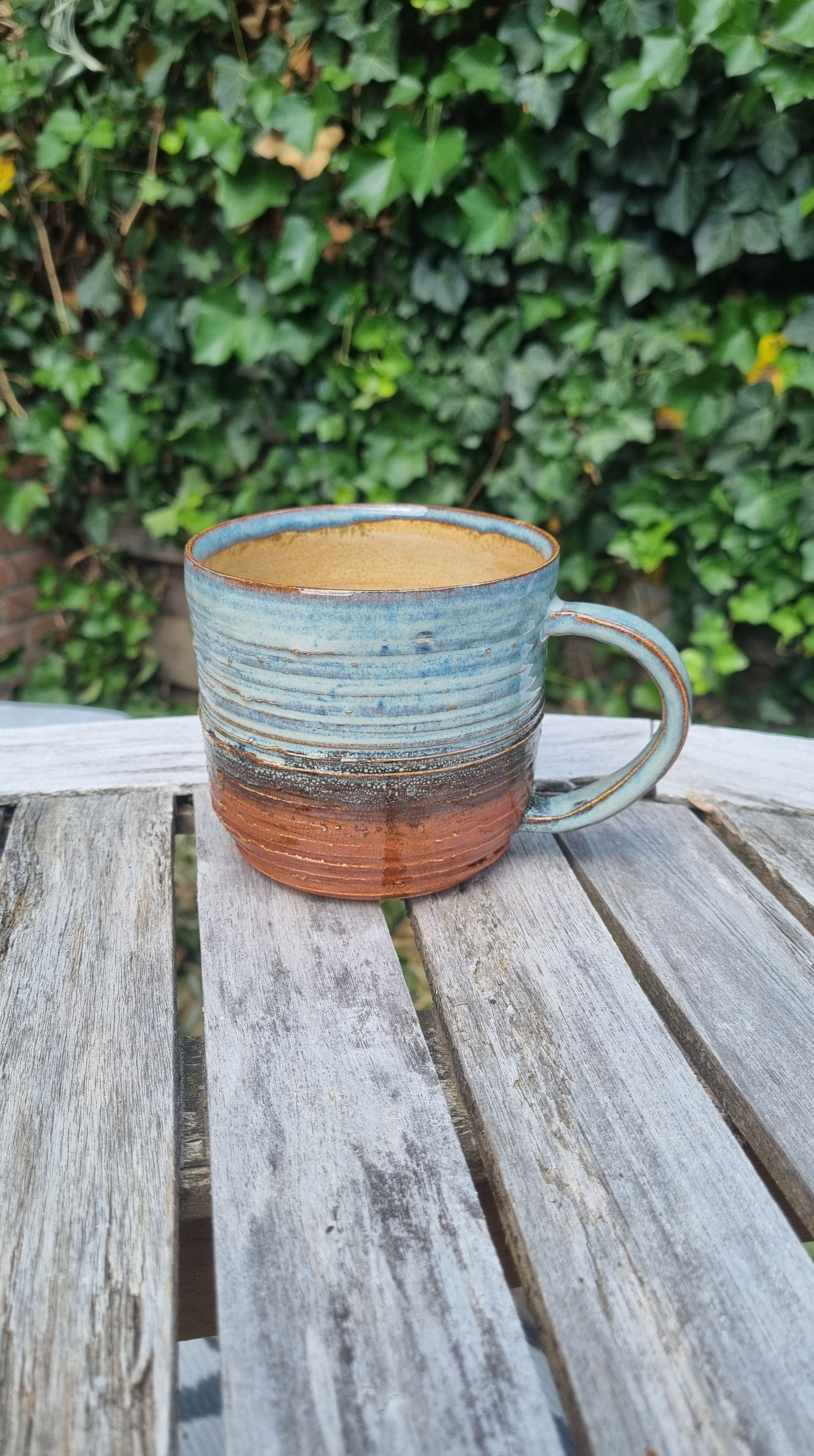 Handgemaakte keramische mok door Mira met roodbruin en blauw twee-kleurig glazuur en handgevormde oor