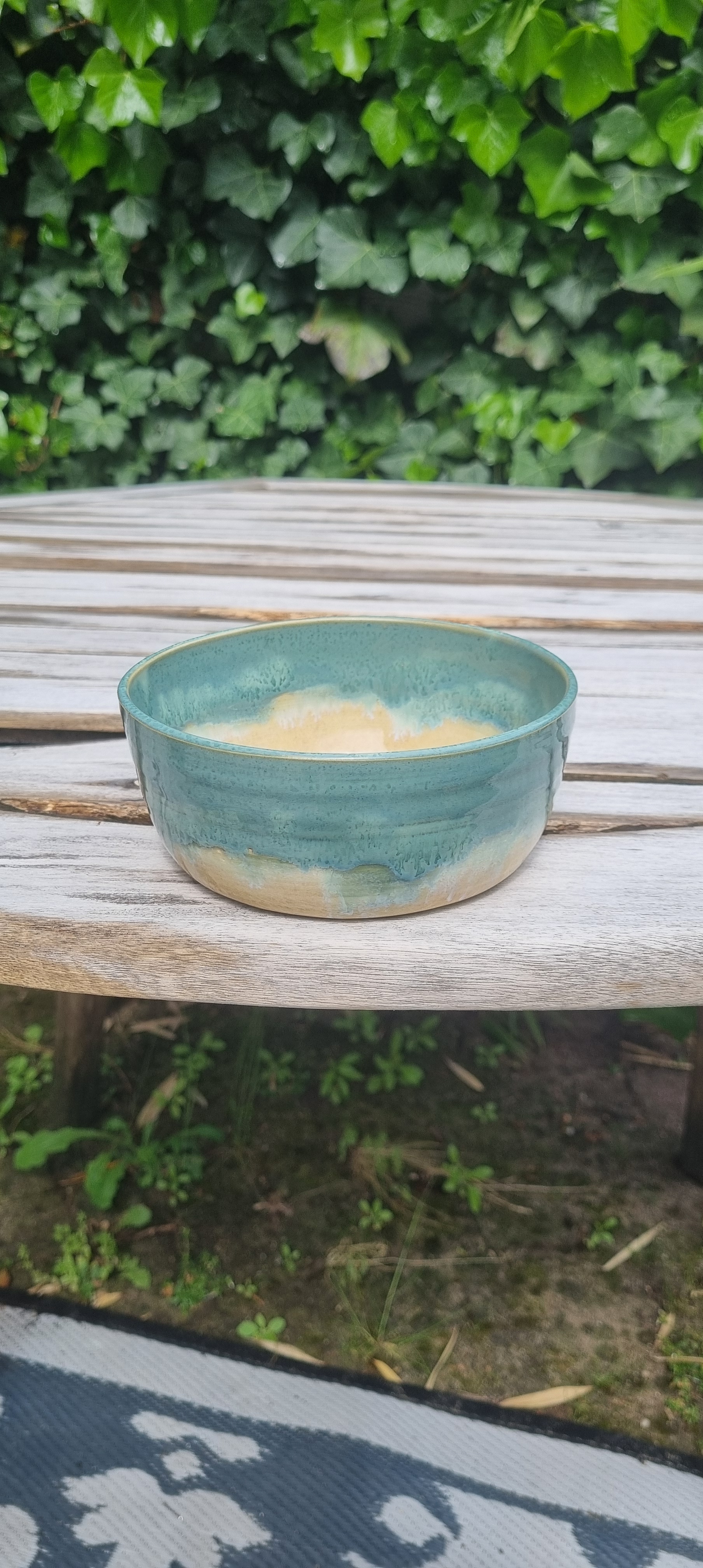 Handgemaakte keramische kom door Mira met turquoise en okergeel glazuur op houten achtergrond buiten